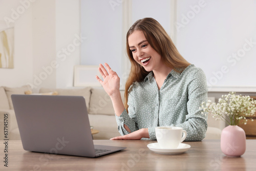 Happy woman having video chat via laptop at wooden table