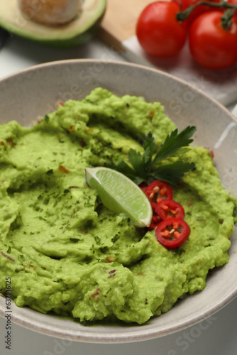 Bowl of delicious guacamole served with lime, pepper and parsley on table