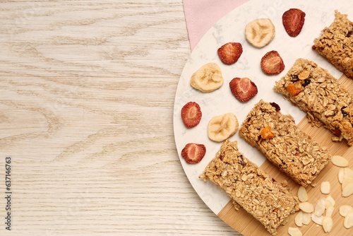 Tasty granola bars, dried strawberries, bananas and almond flakes on wooden table, top view. Space for text