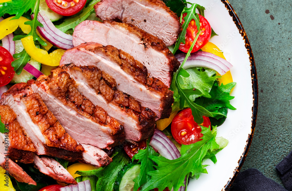 Salad with grilled duck breast slices and cherry tomatoes, cucumber, paprika, red onion, lettuce and arugula on green table background, top view