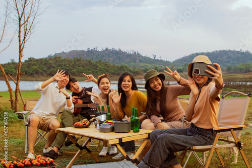 Camping in the evening, sunset behind the mountain with beautiful nature : Young asian gangs of young men and women chatting singing and drinking cold beers happily during an holiday overnight trip.