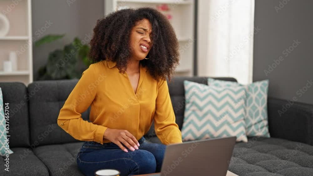 African american woman using laptop suffering for stomach pain at home African american woman using laptop suffering for stomach pain at home