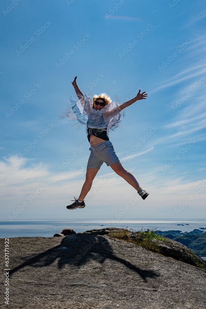 Happy woman is jumping on the top of the mountain. He rejoices at the success of victory over himself, overcoming himself. Hiker on top of Djevelporten, Norway. rock stack in mountain Lofoten Island Happy woman is jumping on the top of the mountain. He rejoices at the success of victory over himself, overcoming himself. Hiker on top of Djevelporten, Norway. rock stack in mountain Lofoten Island