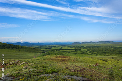 Postcard view of a bright valley and silhouettes of mountains and a blue sky with clouds