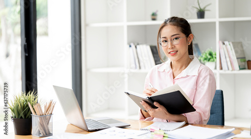 Happy businesswoman working at office desk and analyzing weekly schedule in her notebook