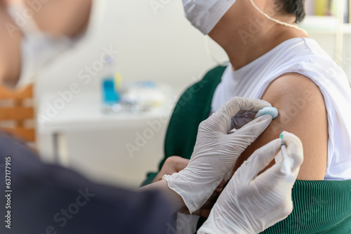 Close up hand of Asian woman nurse injecting covid-19 vaccine to senior Thai woman patient wearing mask in clinic or health care center. Coronavirus pandemic protection or health care medical concept.