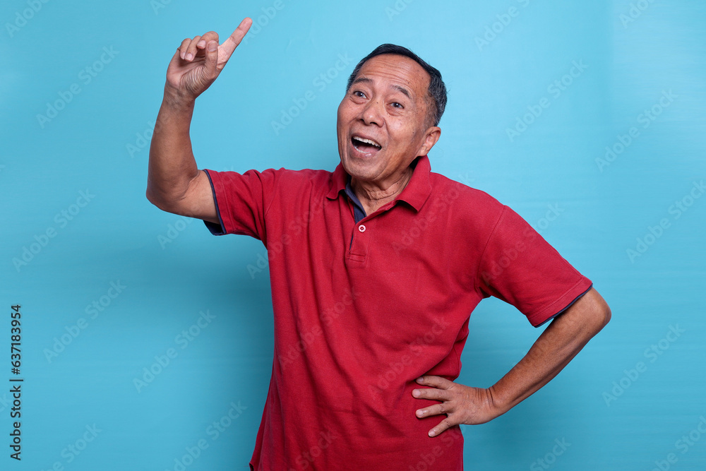 Fototapeta premium Senior Asian male pointing finger up, smiling and happy wearing casual red shirt standing over blue background