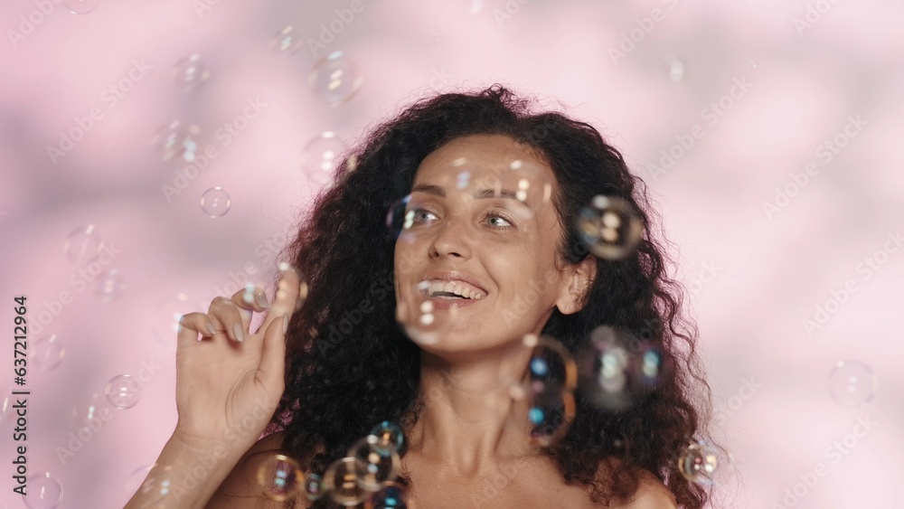 Portrait of a seminude woman in the studio on a pink background with highlights close up. Woman surrounded by soap bubbles. The concept of beauty, cosmetology, skin care, spa, women's health.