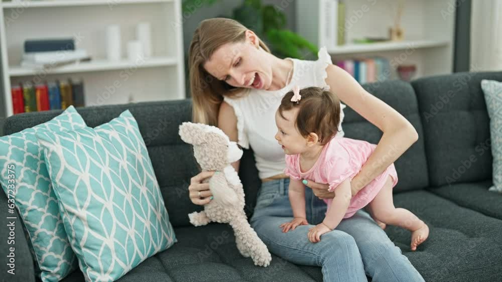 Mother and daughter sitting on sofa playing with teddy bear at home Mother and daughter sitting on sofa playing with teddy bear at home