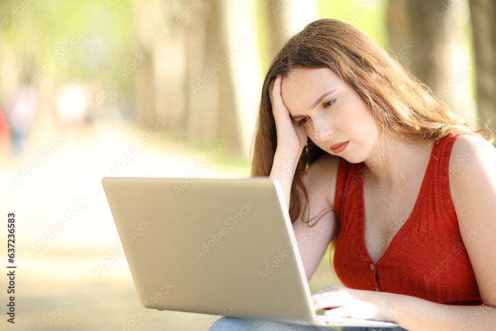 Worried female checking laptop in a park Worried female checking laptop in a park