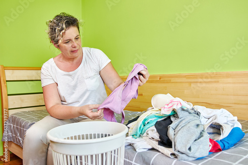Принти на полотні The woman sorts the clothes, and throws the old and worn ones into the trash