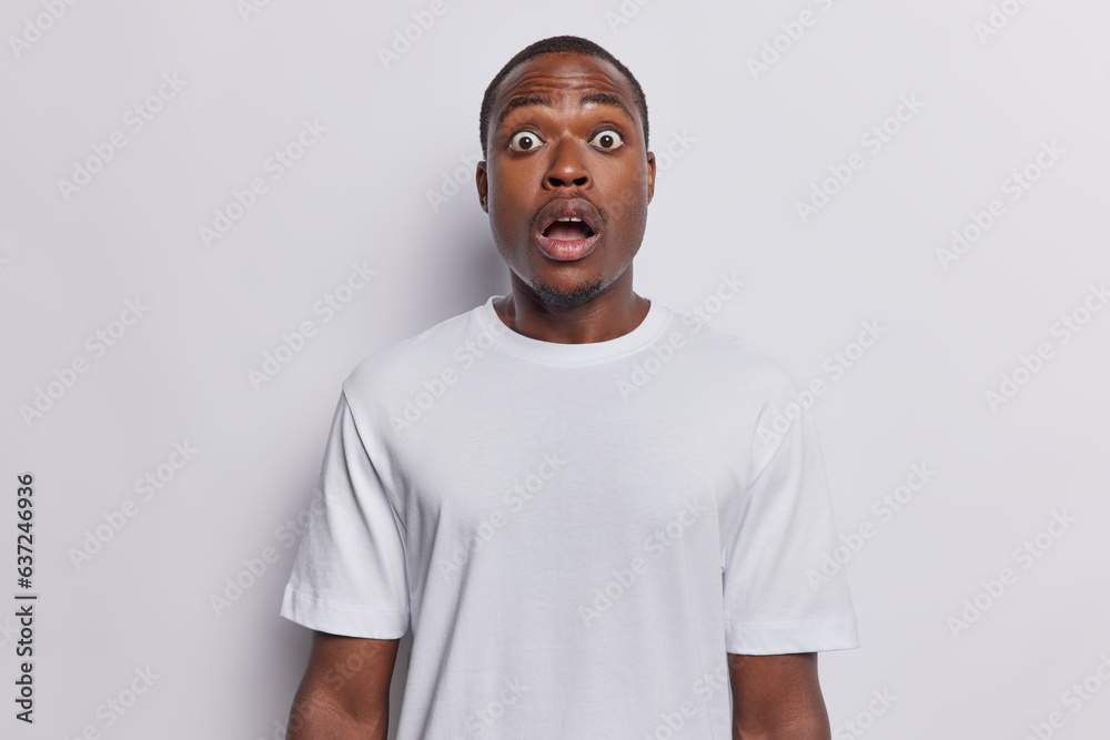 People emotions concept. Studio photo of young surprised Hindu male seeing something unexpected or unusual standing in centre isolated on white background keeping hands down wearing casual t shirt People emotions concept. Studio photo of young surprised Hindu male seeing something unexpected or unusual standing in centre isolated on white background keeping hands down wearing casual t shirt