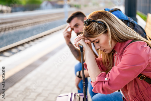 Tired couple sitting at railway station and waiting for arrival of their train.
