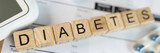 Lettering DIABETES on wooden cubes with pills, glucometer and blood sugar tests on table.