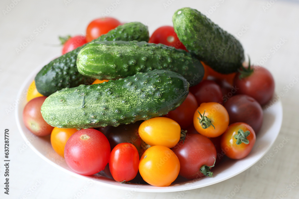 Fresh red, pink and yellow tomatoes and green cucumbers on the white plate Fresh red, pink and yellow tomatoes and green cucumbers on the white plate