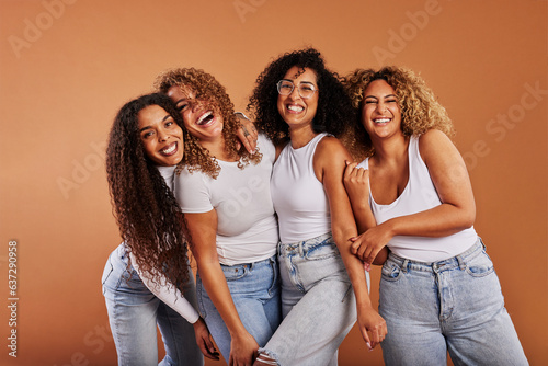 Diverse women in jeans and white tops laughing on an orange background photo