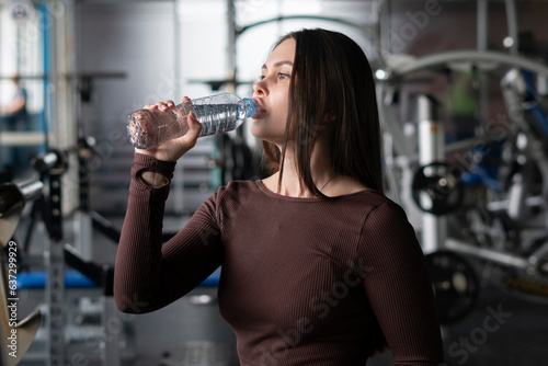young caucasian woman drinking water in a gym, take a break during practice session