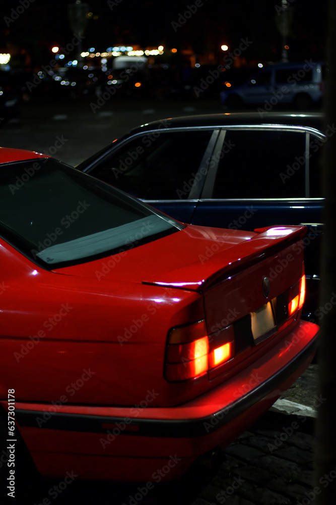 Two old European cars in the city center at night. Black and red car