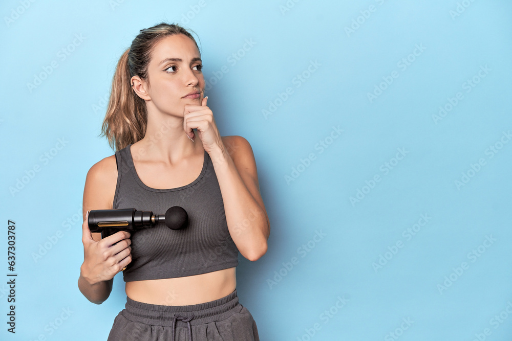 Athlete holding an electric massager looking sideways with doubtful and skeptical expression. Athlete holding an electric massager looking sideways with doubtful and skeptical expression.