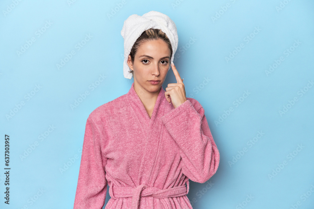 Woman in pink robe after shower pointing temple with finger, thinking, focused on a task. Woman in pink robe after shower pointing temple with finger, thinking, focused on a task.