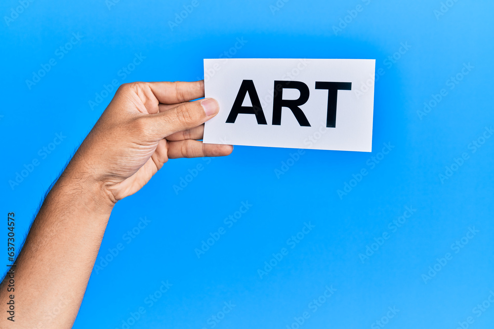 Hand of caucasian man holding paper with art word over isolated blue background Hand of caucasian man holding paper with art word over isolated blue background