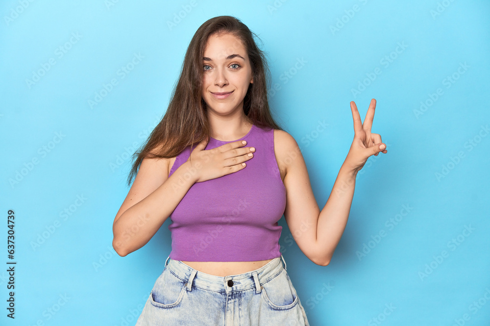 Fashionable young woman in a purple top on blue background taking an oath, putting hand on chest. Fashionable young woman in a purple top on blue background taking an oath, putting hand on chest.
