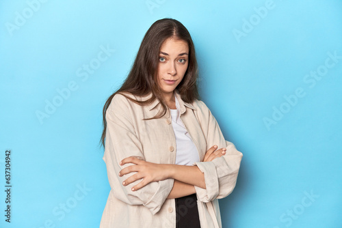 Stylish young woman in an overshirt on a blue background suspicious, uncertain, examining you.