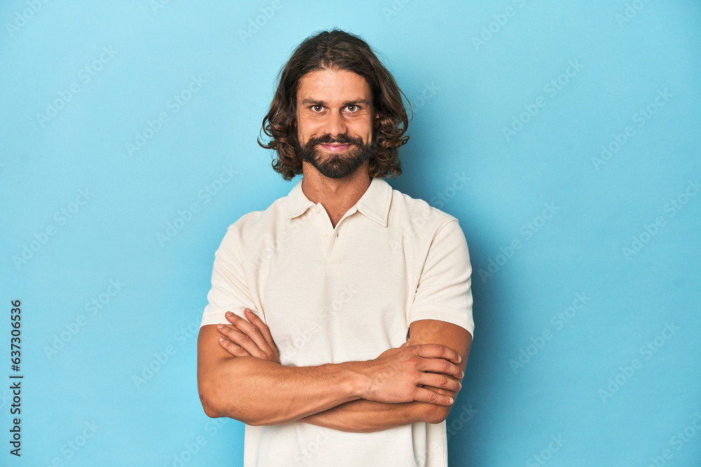 Long-haired man in a white polo, blue studio unhappy looking in camera with sarcastic expression. Long-haired man in a white polo, blue studio unhappy looking in camera with sarcastic expression.