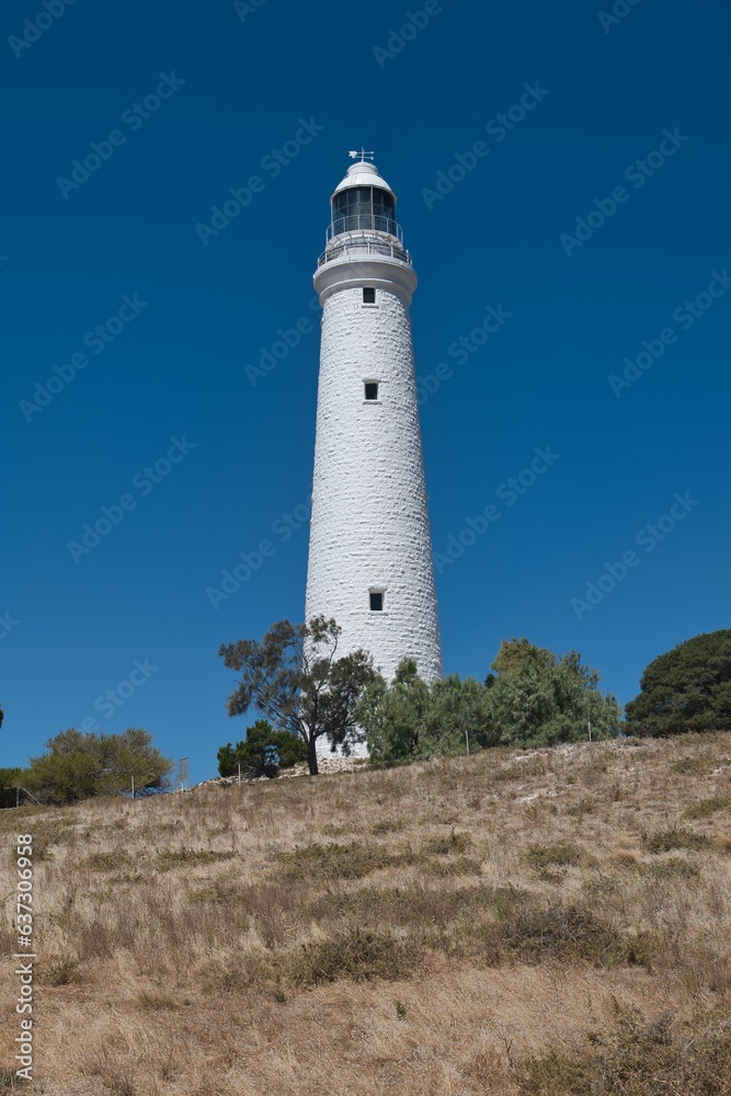 Big white lighthouse on Rottnest Island. Wadjemup Lighthouse at Rottnest Island, Western Australia. Tall white historic lighthouse in front of a perfect blue sky. Western Australia tourist destination