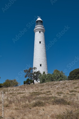 Big white lighthouse on Rottnest Island. Wadjemup Lighthouse at Rottnest Island  Western Australia. Tall white historic lighthouse in front of a perfect blue sky. Western Australia tourist destination