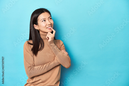 Young Asian woman in brown turtleneck, relaxed thinking about something looking at a copy space.