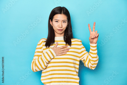 Asian woman in striped yellow sweater, taking an oath, putting hand on chest. © Asier
