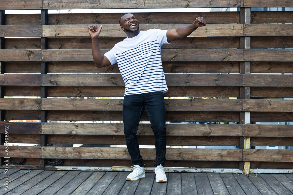 A stylish, young African-American man poses for the camera against the background of a wooden fence