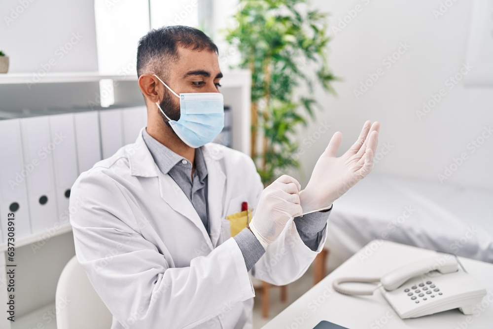 Young hispanic man doctor wearing medical mask wearing gloves at clinic