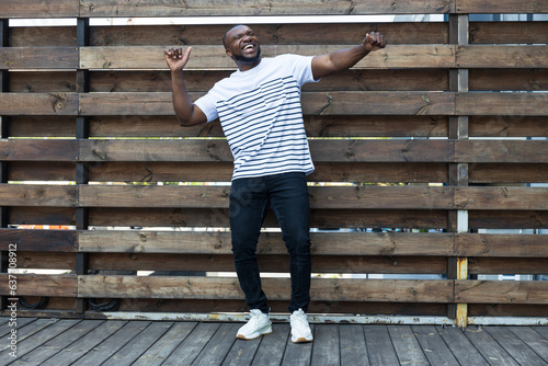 A stylish, young African-American man poses for the camera against the background of a wooden fence