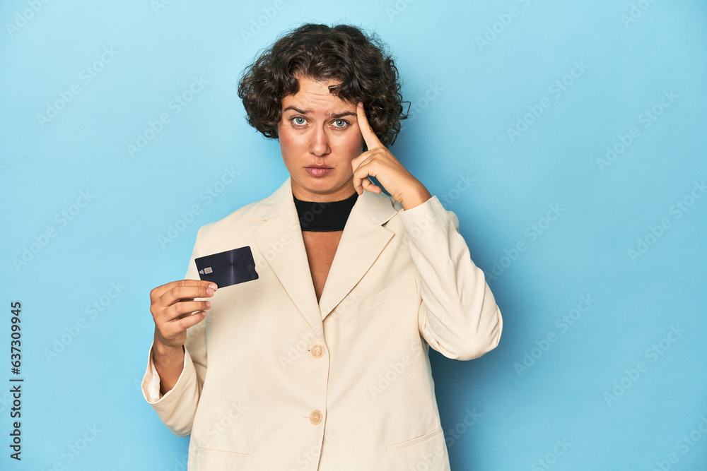 Young woman with credit card, elegant white blazer pointing temple with finger, thinking, focused on a task. Young woman with credit card, elegant white blazer pointing temple with finger, thinking, focused on a task.