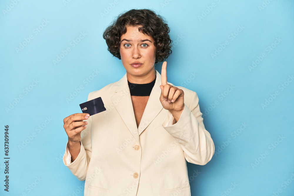 Young woman with credit card, elegant white blazer showing number one with finger. Young woman with credit card, elegant white blazer showing number one with finger.