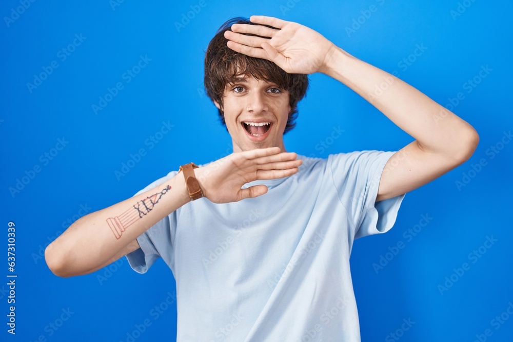 Hispanic young man standing over blue background smiling cheerful playing peek a boo with hands showing face. surprised and exited Hispanic young man standing over blue background smiling cheerful playing peek a boo with hands showing face. surprised and exited