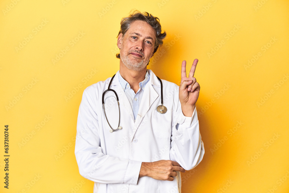 Middle-aged doctor standing against a yellow backdrop showing number two with fingers. Middle-aged doctor standing against a yellow backdrop showing number two with fingers.