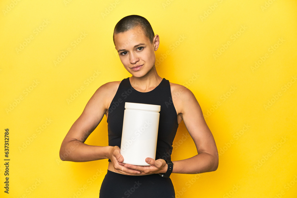 Sportswoman holding protein shake bottle, yellow studio backdrop Sportswoman holding protein shake bottle, yellow studio backdrop