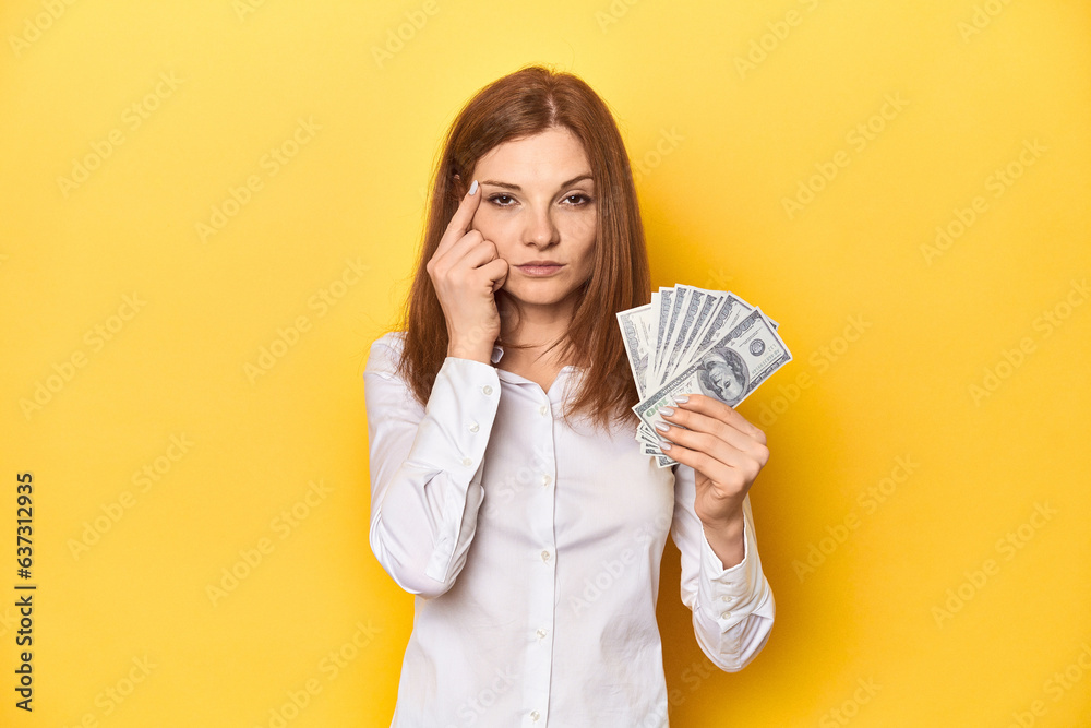 Redhead with dollar bills, cash in hand showing a disappointment gesture with forefinger. Redhead with dollar bills, cash in hand showing a disappointment gesture with forefinger.