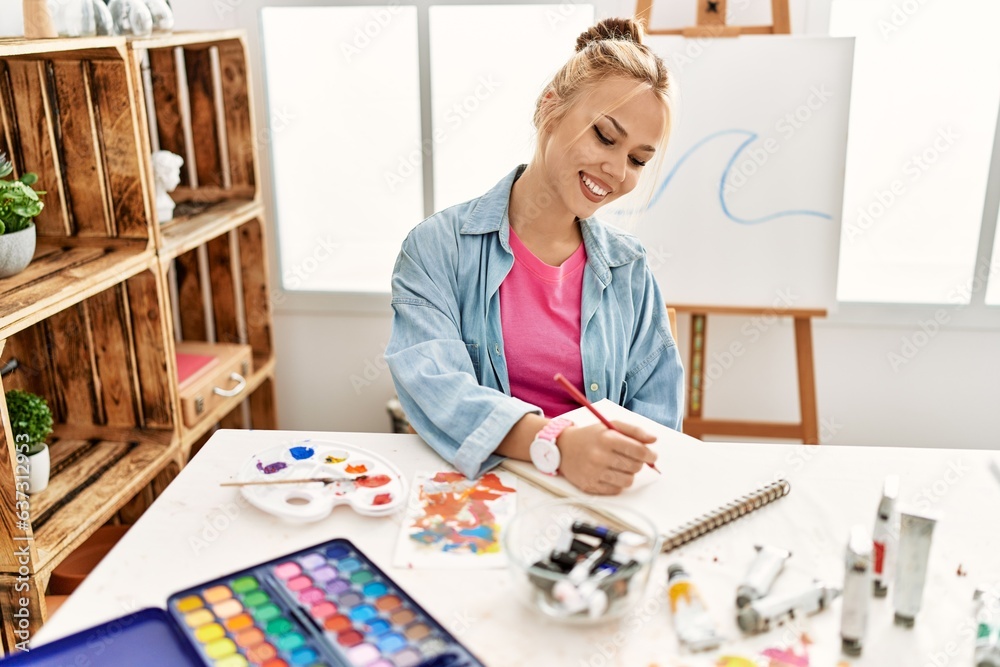 Young caucasian woman artist smiling confident drawing on notebook at art studio