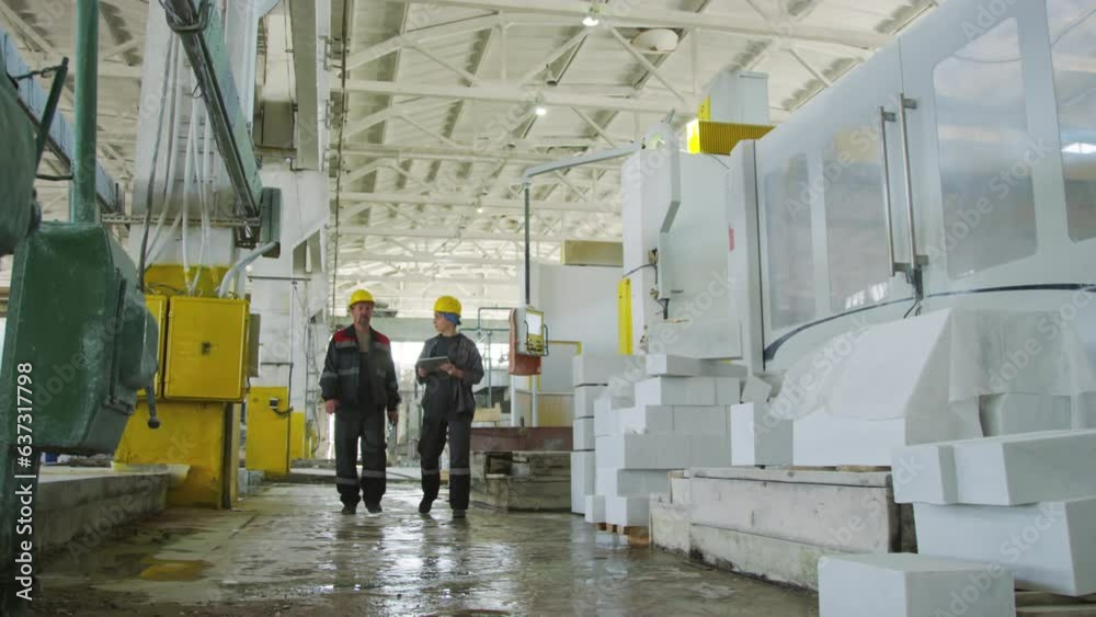 Wide shot of male and female coworkers in hardhats and uniform using digital tablet and speaking while walking through industrial factoryWide shot of male and female coworkers in hardhats and uniform Wide shot of male and female coworkers in hardhats and uniform using digital tablet and speaking while walking through industrial factoryWide shot of male and female coworkers in hardhats and uniform