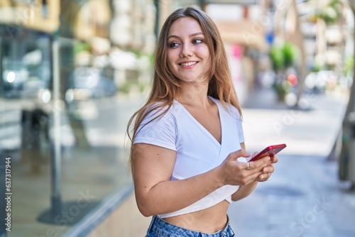 Young blonde woman smiling confident using smartphone at street