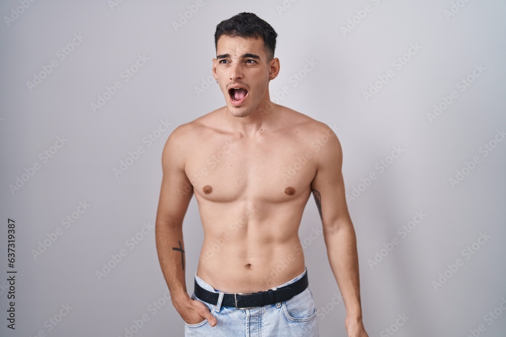 Handsome hispanic man standing shirtless angry and mad screaming frustrated and furious, shouting with anger. rage and aggressive concept.