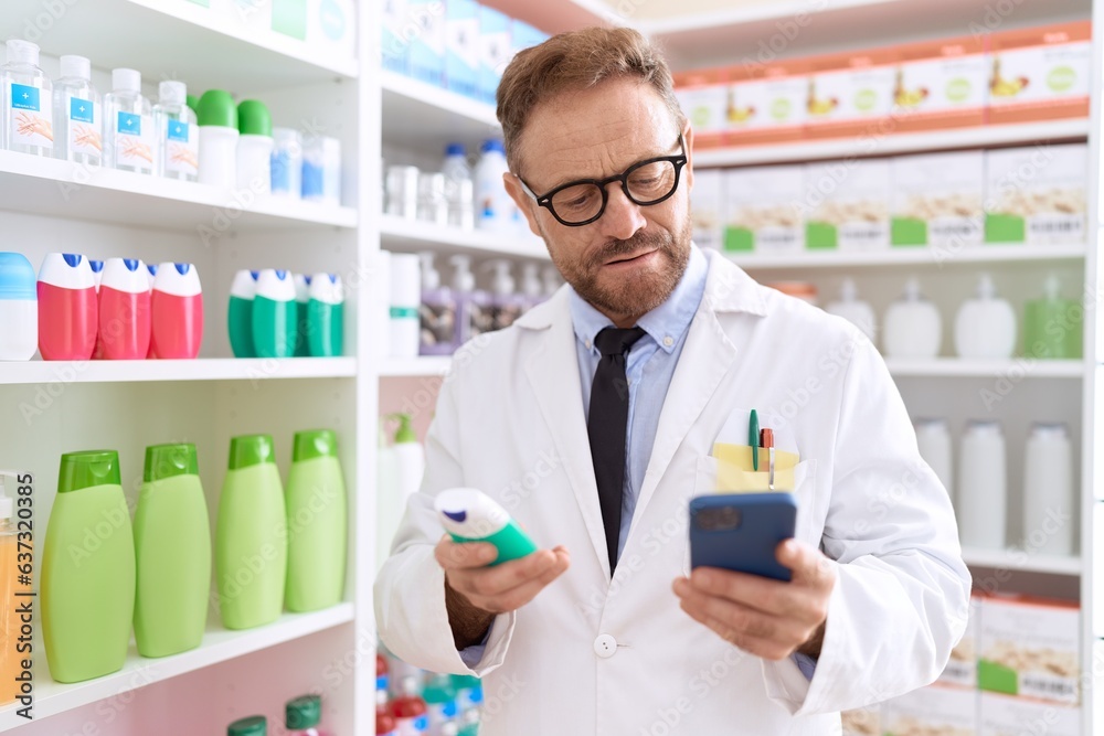 Middle age man pharmacist using smartphone holding toothpaste at pharmacy