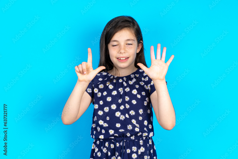 caucaisna kid girl wearing floral dress over blue background showing and pointing up with fingers number seven while smiling confident and happy.
