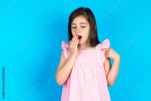 Shocked caucaisna kid girl wearing pink dress over blue background look surprisedly down, indicates at blank  with fore finger, Scared model