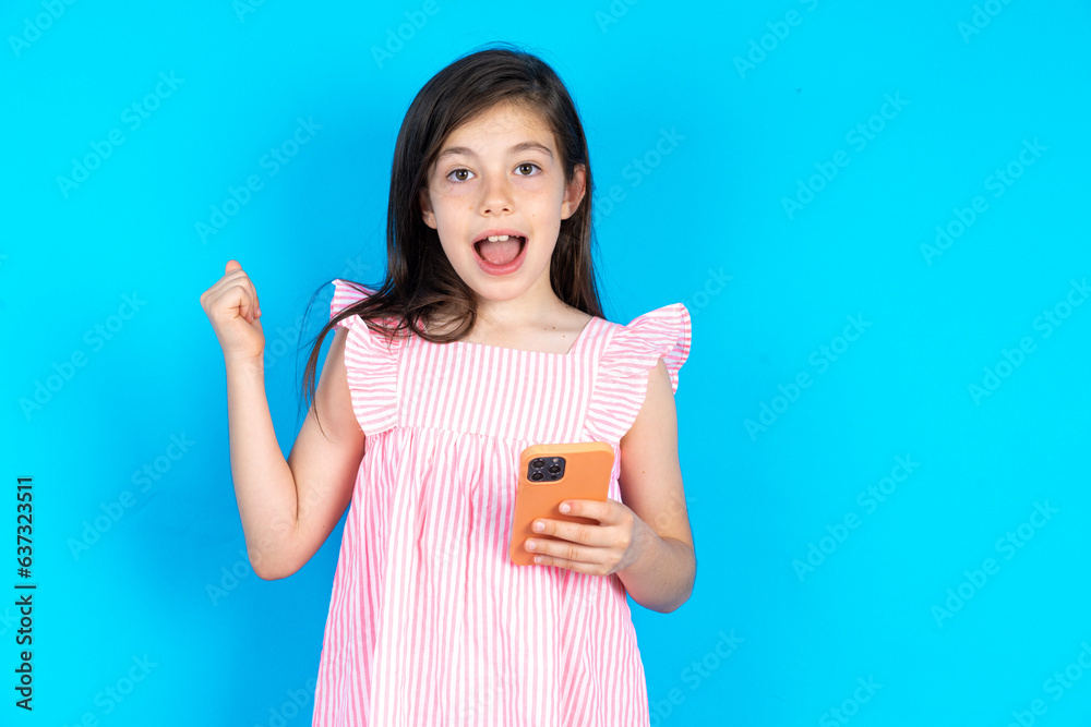 Portrait of caucaisna kid girl wearing pink dress over blue background holding in hands cell celebrating Portrait of caucaisna kid girl wearing pink dress over blue background holding in hands cell celebrating
