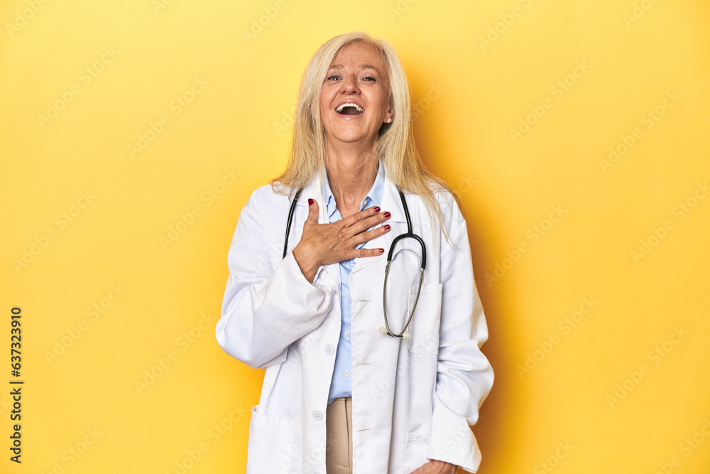Middle-aged Caucasian female doctor on yellow studio backdrop Middle-aged Caucasian female doctor on yellow studio backdroplaughs out loudly keeping hand on chest. Middle-aged Caucasian female doctor on yellow studio backdrop Middle-aged Caucasian female doctor on yellow studio backdroplaughs out loudly keeping hand on chest.